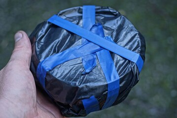 hand holds a round box in black cellophane wrapped in blue electrical tape on a gray background