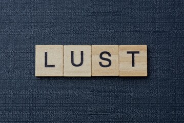 gray word lust from small wooden letters on a black table