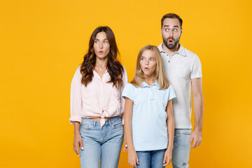 Fototapeta premium Shocked amazed young parents mom dad with child kid daughter teen girl in basic t-shirts keeping mouth open looking aside isolated on yellow background studio portrait. Family day parenthood concept.