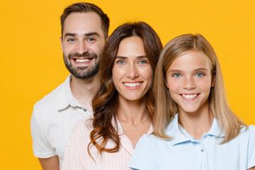 Smiling cheerful young happy parents mom dad with child kid daughter teen girl in basic t-shirts looking camera isolated on yellow background studio portrait. Family day parenthood childhood concept.