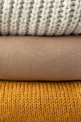 Knitted sweaters folded in a stack, close-up. Autumn or winter vertical background