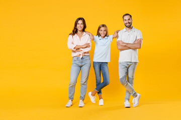 Fototapeta premium Full length portrait smiling young parents mom dad with child kid daughter teen girl in basic t-shirts jumping holding hands crossed isolated on yellow background studio portrait. Family day concept.