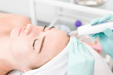 The female cosmetologist makes  a procedure of ultrasonic cleaning face, close-up. Young woman in a beauty salon. Concept of cosmetology and professional skin care