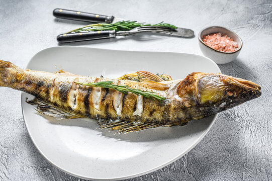 Grilled Zander, walleye fish with herbs and lemon on a plate. Gray wooden background. Top view