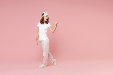 Fototapeta na wymiar Full length side view portrait of cheerful young woman in white pajamas home wear sleep mask point thumb aside on mock up copy space rest at home isolated on pink background. Relax good mood concept.