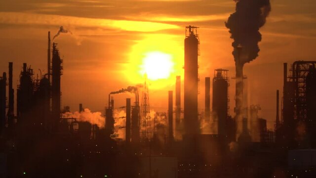 Smoke emission from pipes of an oil refinery in the backlight of the sunset.