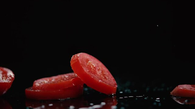 Ruedas de tomate cayendo en splash en lamina negra salpicando agua. HD