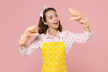 Cheerful young woman housewife in yellow apron gloves potholders showing blah blah gesture ja jaja hands while doing housework isolated on pastel pink background studio portrait. Housekeeping concept. © ViDi Studio