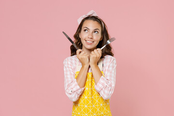 Smiling young brunette woman housewife 20s wearing yellow apron hold knife and fork looking up...