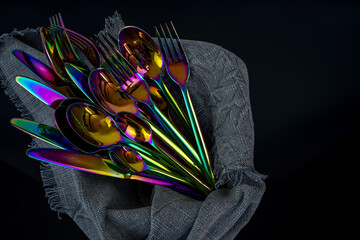A bunch of stylish colored cutlery on a dark grey linen napkin. Dark and moody vibes. Fashionable and luxury eating.
