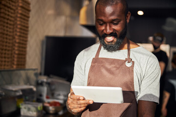 Jolly male chef using tablet in kitchen