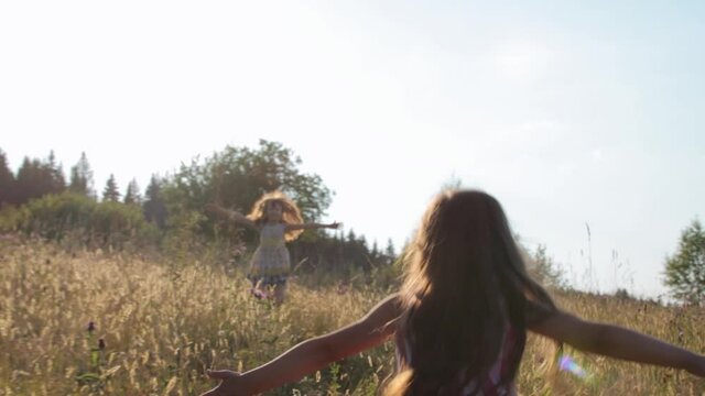 Two little girs running through summer field and embracing each other