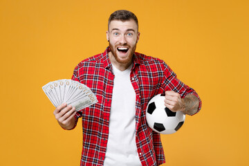 Joyful young man football fan cheer up support favorite team with soccer ball hold cash money in...