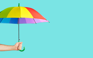 Rainbow-colored umbrella in male hand on green background