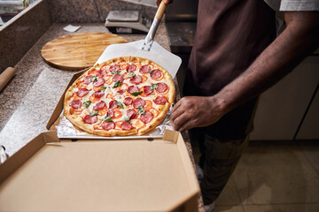 Young man placing pepperoni pizza in paper box