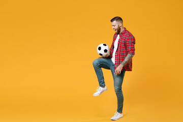Full length portrait of excited young man football fan in red shirt cheer up support favorite team juggling soccer ball on knee soccer ball isolated on yellow background. People sport leisure concept.
