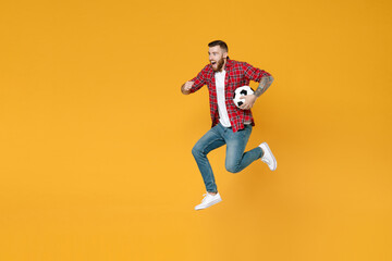 Fototapeta na wymiar Full length portrait of excited young man football fan in red shirt cheer up support favorite team with soccer ball jumping like running isolated on yellow background. People sport leisure concept.