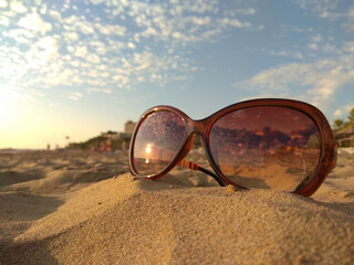 Fototapeta na wymiar Sunglasses in the sand on shore. Concept: tourism, beach vacation, travel. Reflection of the setting sun