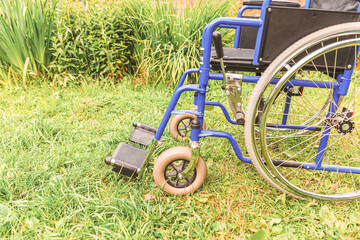 Empty wheelchair standing on grass in hospital park waiting for patient services. Invalid chair for disabled people parked outdoor in nature. Handicap accessible symbol. Health care medical concept.
