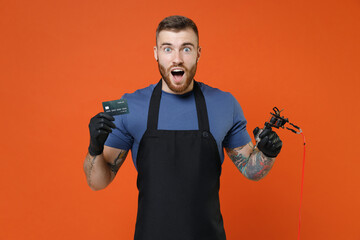Amazed professional tattooer master artist tattooed man in apron hold credit bank card machine...