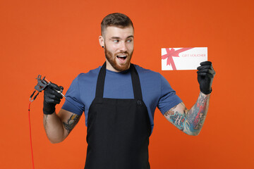 Amazed professional tattooer master artist tattooed man in apron hold gift certificate machine...