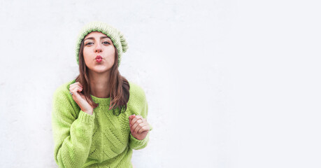 Woman in a knitted sweater and har sending an air kiss. Blank space for text on the background