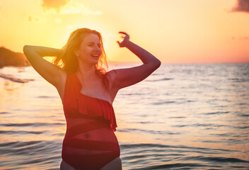 Fototapeta na wymiar carefree woman in red swimsuit dancing at sunset on the beach. mature woman relaxation vitality healthy lifestyle. Copy space