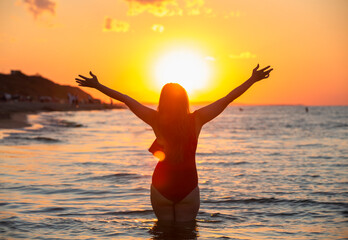 Black silhouette of a woman in a swimsuit on the background of the ocean. happy young woman on sea background enjoying freedom with open hands at sunset