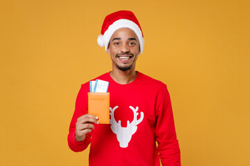 Smiling young african american traveler tourist Santa man wearing sweater Christmas hat hold passport tickets isolated on yellow background studio portrait. Happy New Year celebration holiday concept.