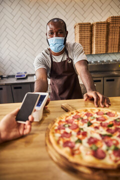 Male Pizzeria Worker In Medical Mask Using Terminal For Contactless Payment