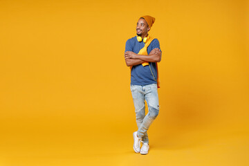 Fototapeta na wymiar Full length of smiling attractive young african american man 20s wearing blue t-shirt hat standing holding hands crossed looking aside isolated on bright yellow colour background, studio portrait.