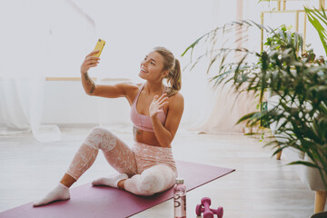 Smiling young strong sporty fitness woman wearing pink tracksuit doing yoga exercises sitting...