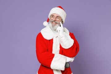 Fototapeta na wymiar Pensive Santa Claus man in Christmas hat red suit coat glasses put hand prop up on chin looking aside isolated on violet purple background studio. Happy New Year celebration merry holiday concept.