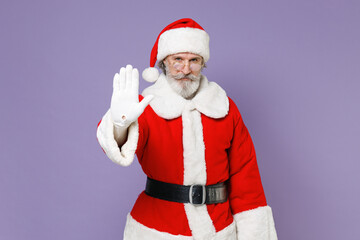 Fototapeta na wymiar Dissatisfied Santa Claus man in Christmas hat red suit coat white gloves glasses showing stop gesture with palm isolated on violet background studio. Happy New Year celebration merry holiday concept.