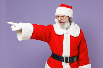 Fototapeta na wymiar Angry Santa Claus man in Christmas hat red suit coat white gloves glasses point index finger aside swearing screaming isolated on violet background. Happy New Year celebration merry holiday concept.