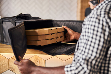Afro American young man putting pizza boxes in delivery bag