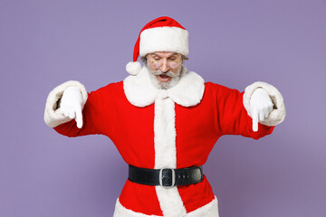 Shocked gray-haired Santa Claus man in Christmas hat red suit coat gloves glasses pointing index fingers down isolated on violet background studio. Happy New Year celebration merry holiday concept.