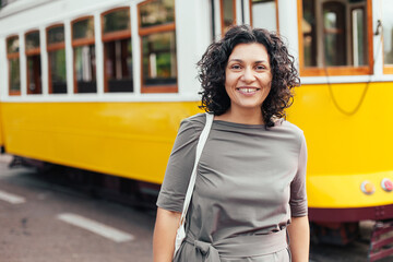 Woman with curly hair in a dress walking in Lisbon, yellow tram on the background