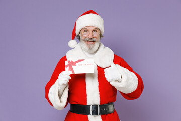 Fototapeta na wymiar Excited elderly Santa Claus man in Christmas hat red suit coat gloves glasses hold gift certificate showing thumb up isolated on violet background. Happy New Year celebration merry holiday concept.
