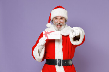 Fototapeta na wymiar Funny Santa Claus man in Christmas hat red suit coat gloves glasses hold gift certificate point index finger on camera isolated on violet background. Happy New Year celebration merry holiday concept.