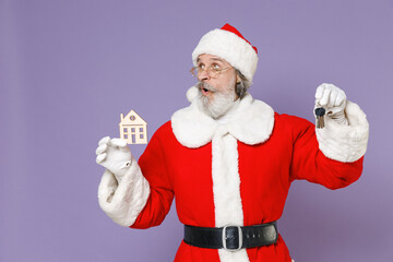 Fototapeta na wymiar Shocked Santa Claus man in Christmas hat red suit coat white gloves glasses holding house and bunch of apartment keys isolated on violet background. Happy New Year celebration merry holiday concept.