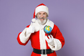 Fototapeta na wymiar Smiling Santa Claus man in Christmas hat red suit coat gloves glasses hold Earth world globe showing thumb up isolated on violet background studio. Happy New Year celebration merry holiday concept.