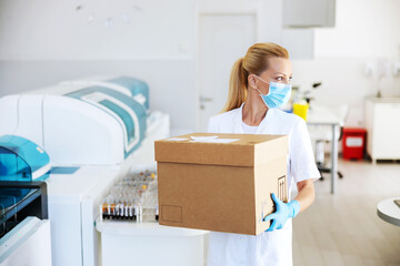 Attractive positive blond lab assistant carrying box with vaccines for Covid 19. Laboratory...
