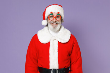 Smiling funny elderly gray-haired Santa Claus man in Christmas hat red suit coat glasses looking camera isolated on violet purple background studio. Happy New Year celebration merry holiday concept.