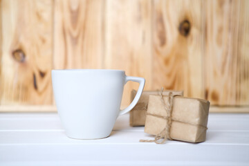 Mock up of white cup on the wooden table, place for a text. Presents and pines.