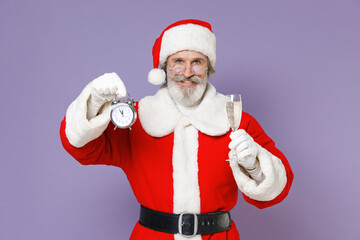 Fototapeta na wymiar Smiling Santa Claus man in Christmas hat red suit coat white gloves glasses hold alarm clock glass of champagne isolated on violet background studio. Happy New Year celebration merry holiday concept.