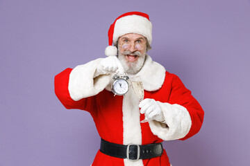 Fototapeta na wymiar Excited Santa Claus man in Christmas hat red suit coat white gloves glasses hold alarm clock glass of champagne isolated on violet background studio. Happy New Year celebration merry holiday concept.