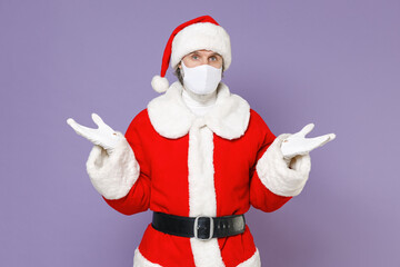 Santa Claus man in Christmas hat suit face mask safe from coronavirus virus covid-19 during quarantine spreading hands isolated on violet background. Happy New Year celebration merry holiday concept.