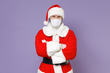 Fototapeta na wymiar Santa Claus man in Christmas hat red coat suit face mask to safe from coronavirus virus covid-19 holding hands crossed isolated on violet background. Happy New Year celebration merry holiday concept.