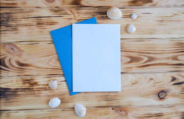 White greeting card mock up on the wooden table with craft envelope, seashells, place for a text.